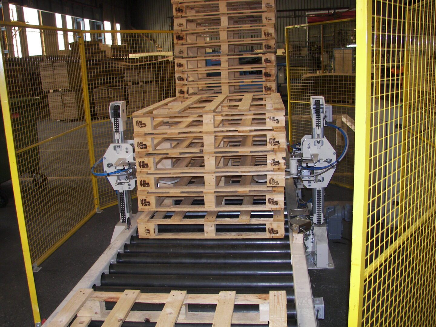 Convoyeur à palettes à rouleaux avec empileur de palettes en bois, utilisé dans un environnement industriel pour le stockage et le transport de palettes.