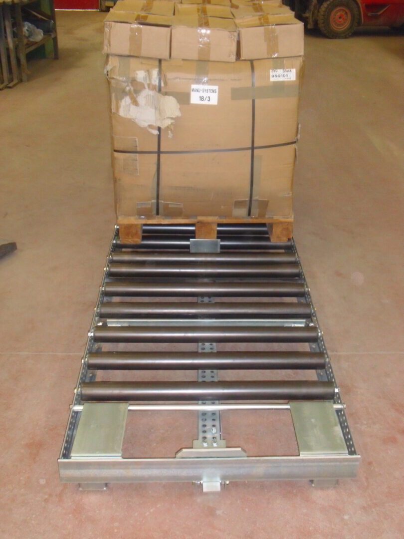 Ligne de stockage dynamique pour picking avec une palette de cartons posée sur des rouleaux métalliques.