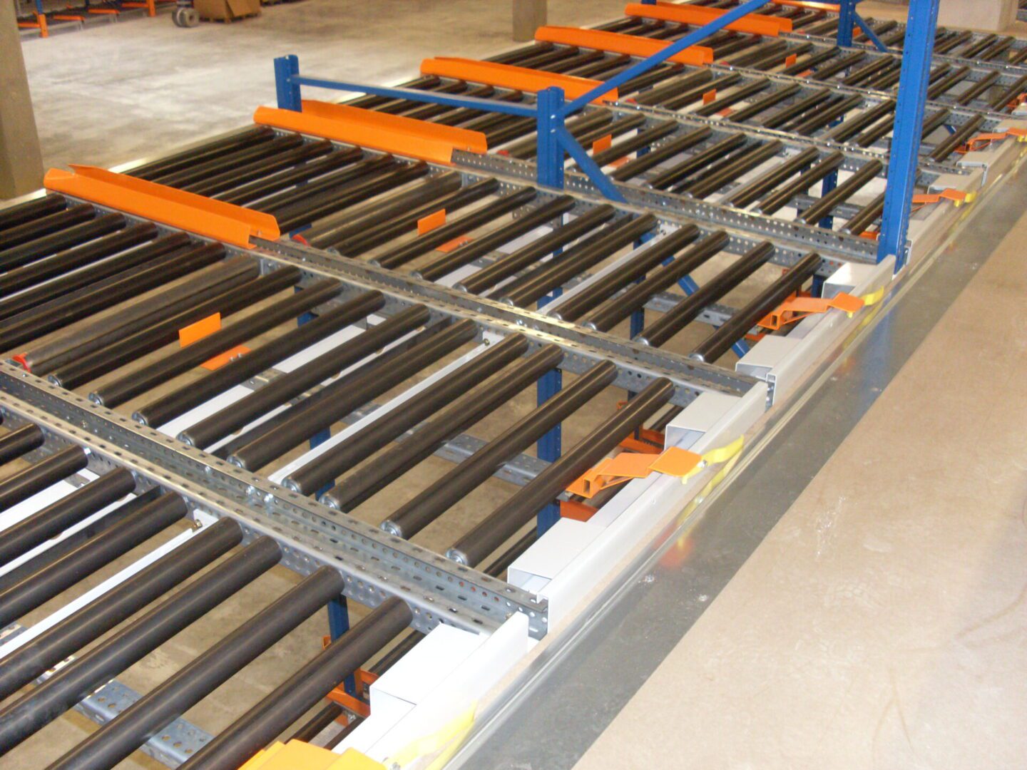 Ligne de stockage dynamique pour picking avec des rouleaux métalliques noirs et des supports orange dans un entrepôt.