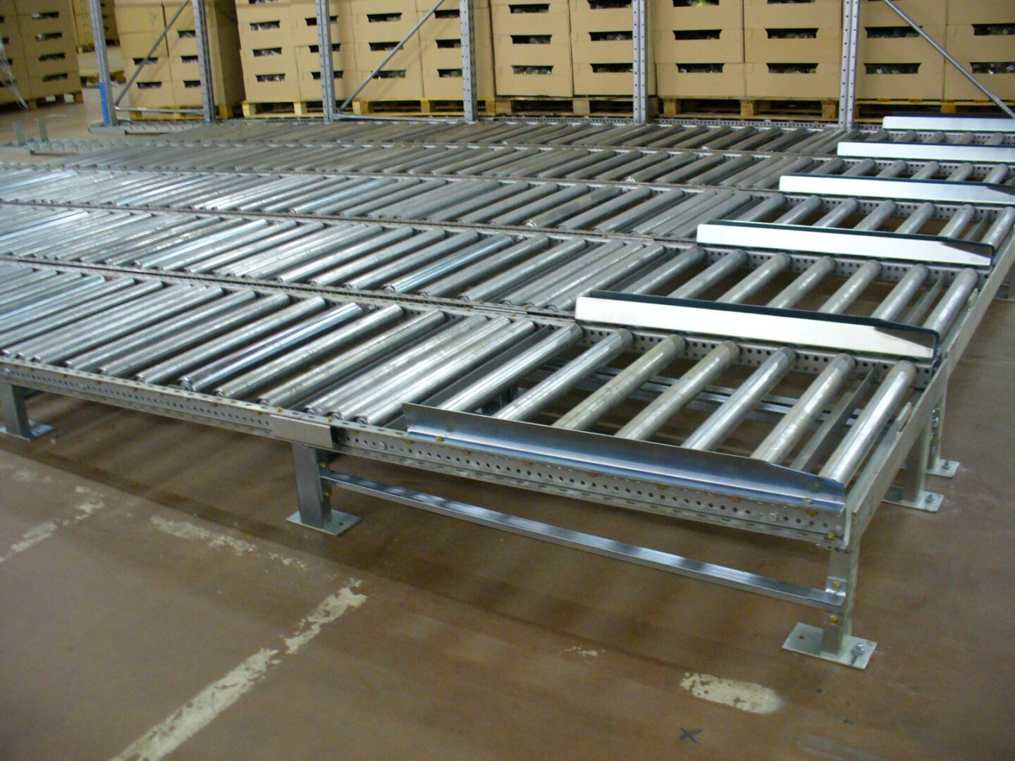 Système de stockage dynamique pour palettes dans un environnement de stockage au froid, avec des rouleaux métalliques devant des étagères de cartons.