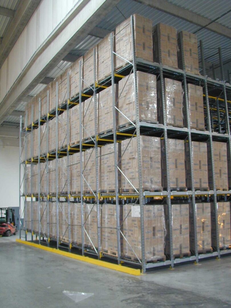 Système de stockage dynamique de palettes sur mesure dans un entrepôt, avec des étagères métalliques hautes et des palettes empilées.